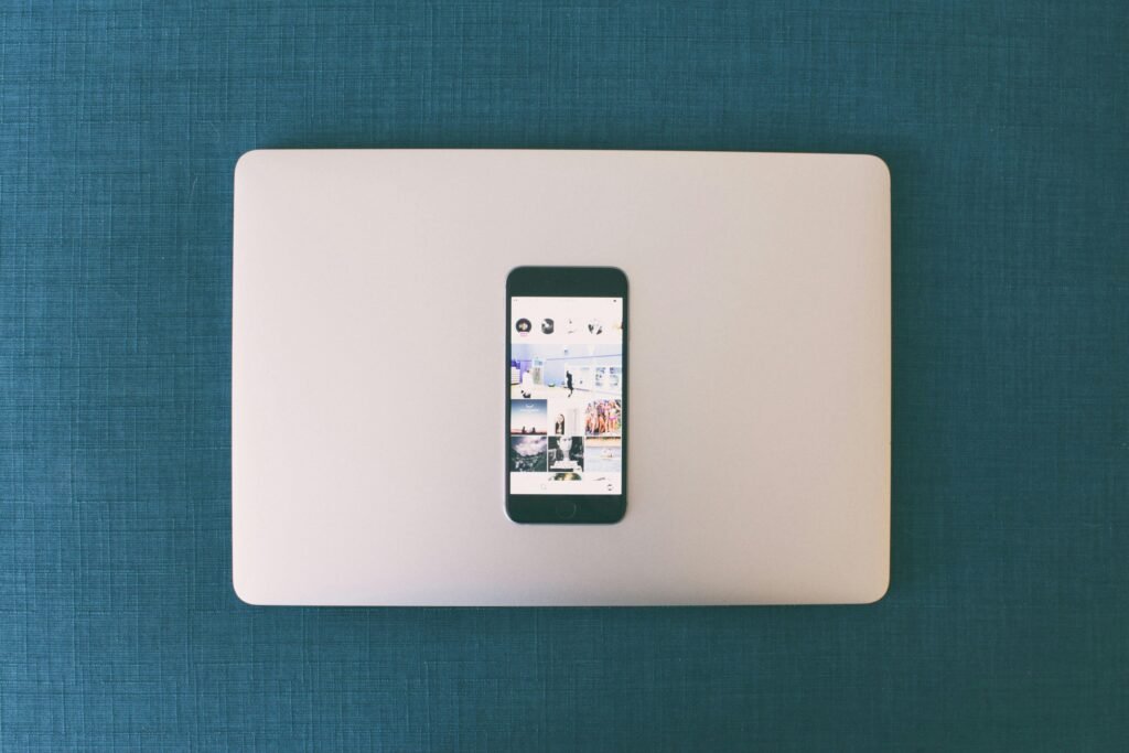 Flat lay of a smartphone on a laptop with social media photos on screen.